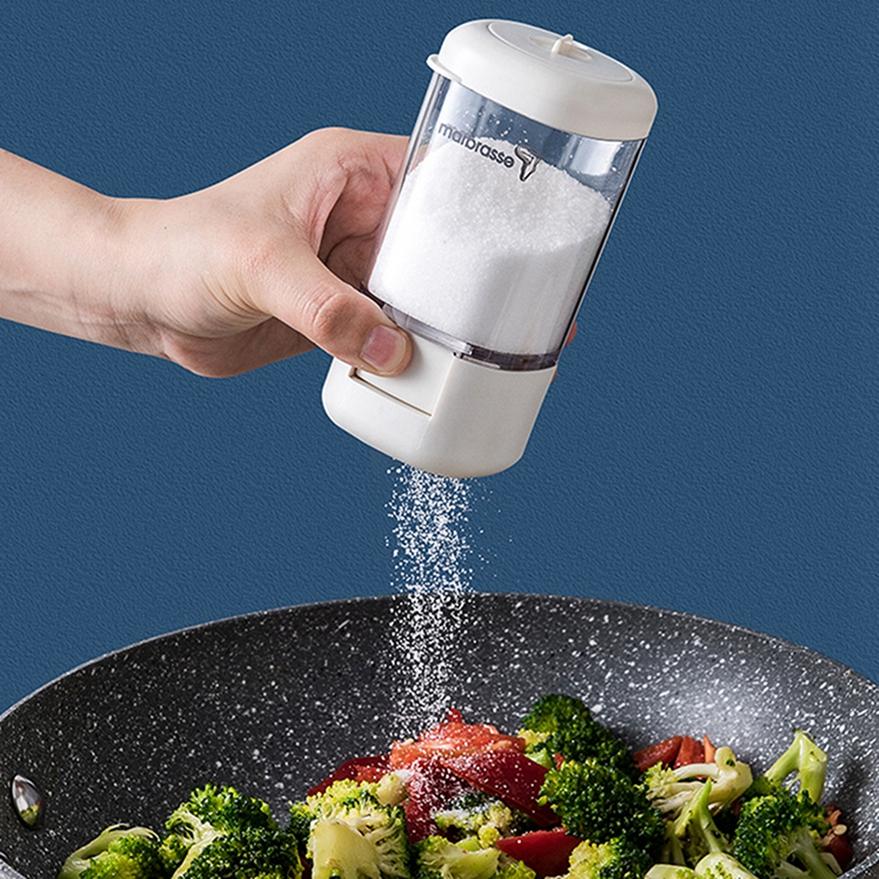 Dosatore per spezie a pressione in mano con coperchio bianco e barattolo trasparente