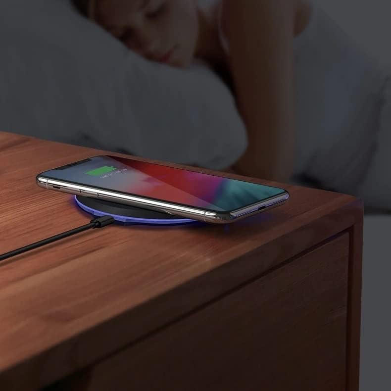 Pad di ricarica wireless nero con smartphone in carica su piano in legno.