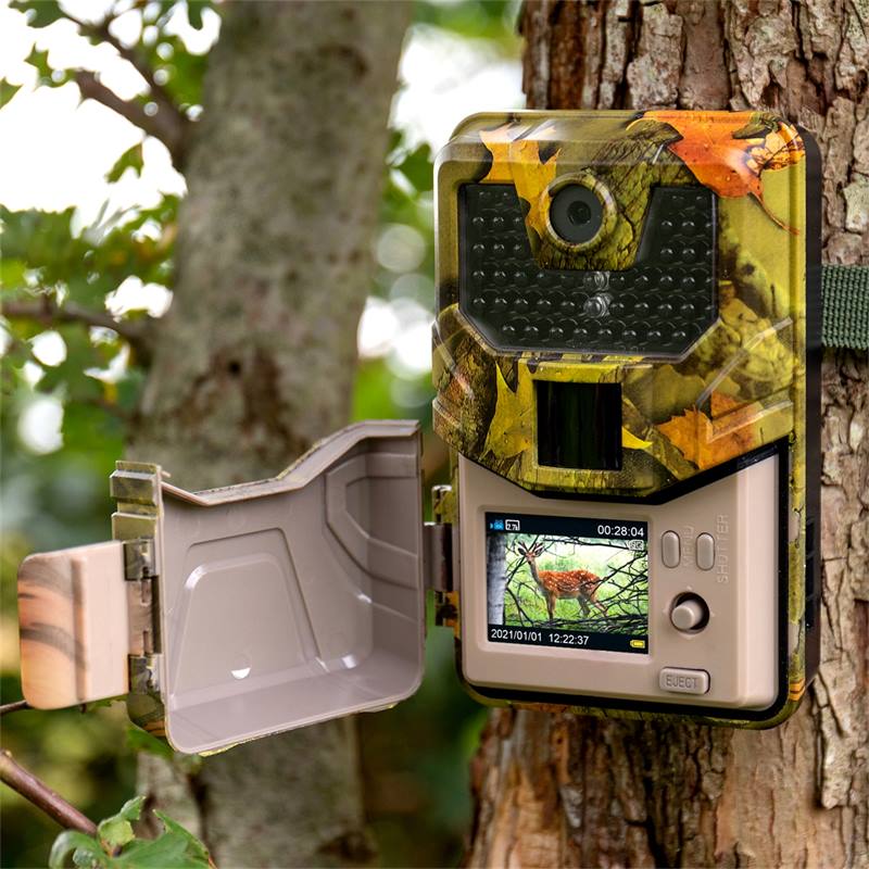Fototrappola mimetica con schermo LCD aperto e telecamera frontale vicino a un albero