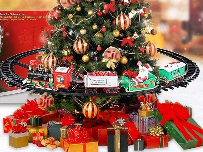 Trenino natalizio con 3 vagoni rossi e verdi sul cerchio di binari attorno all’albero.