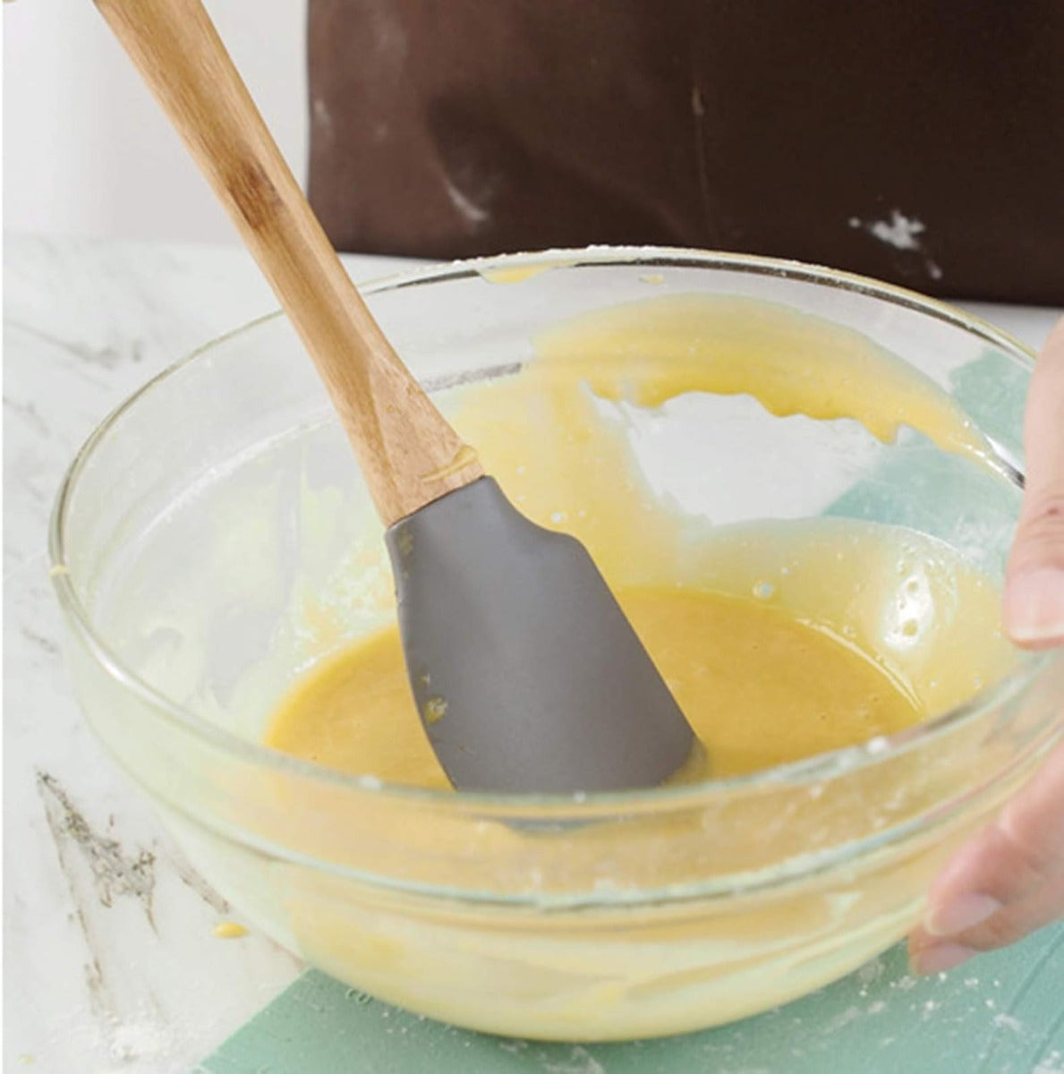 Spatola in silicone grigio con manico in legno, in ciotola con impasto giallo