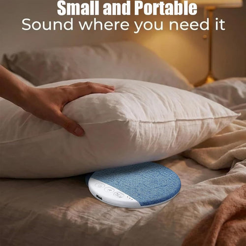 Altoparlante tondo in tessuto blu con base bianca, appoggiato su cuscino e letto.