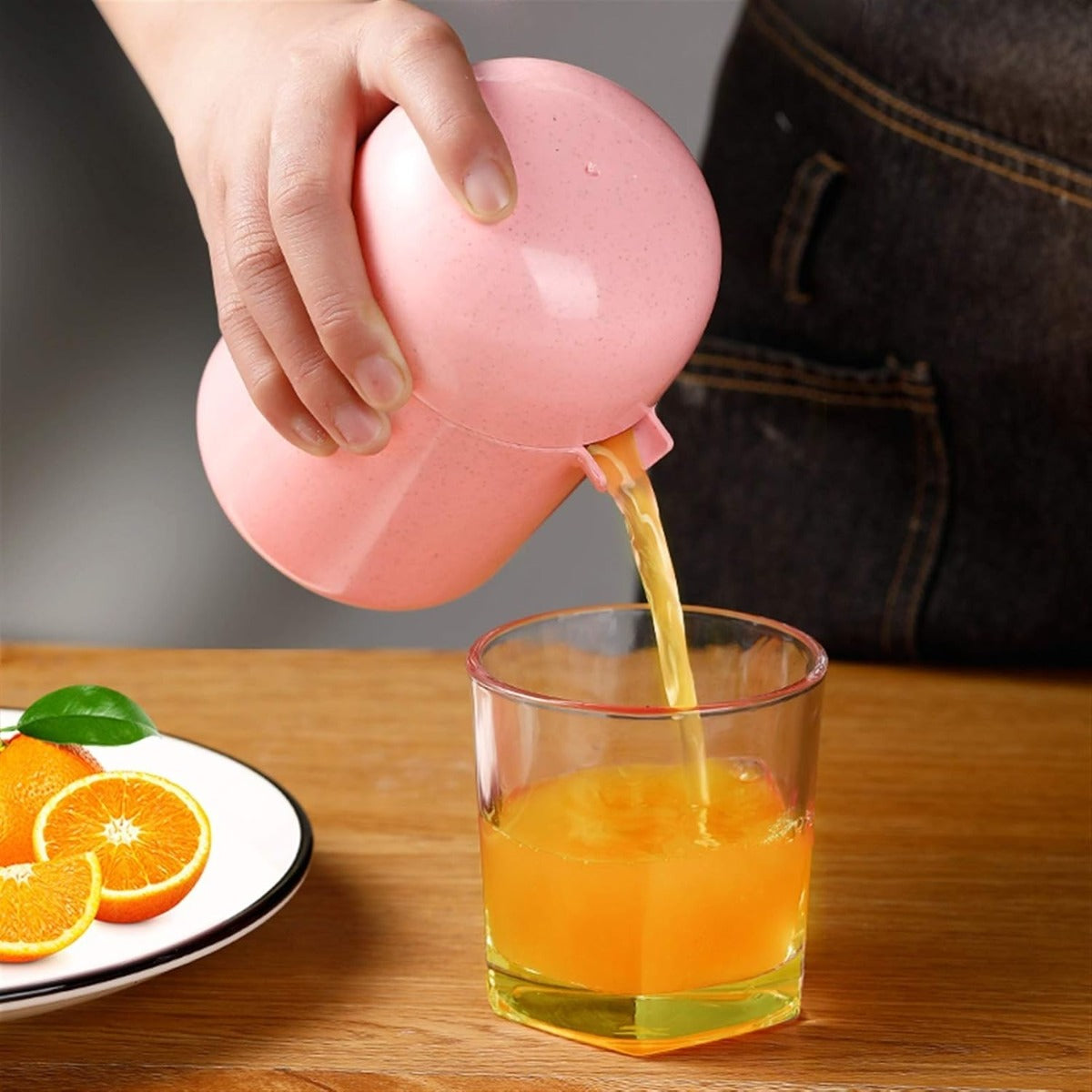 Spremiagrumi manuale rosa mentre versa succo in un bicchiere