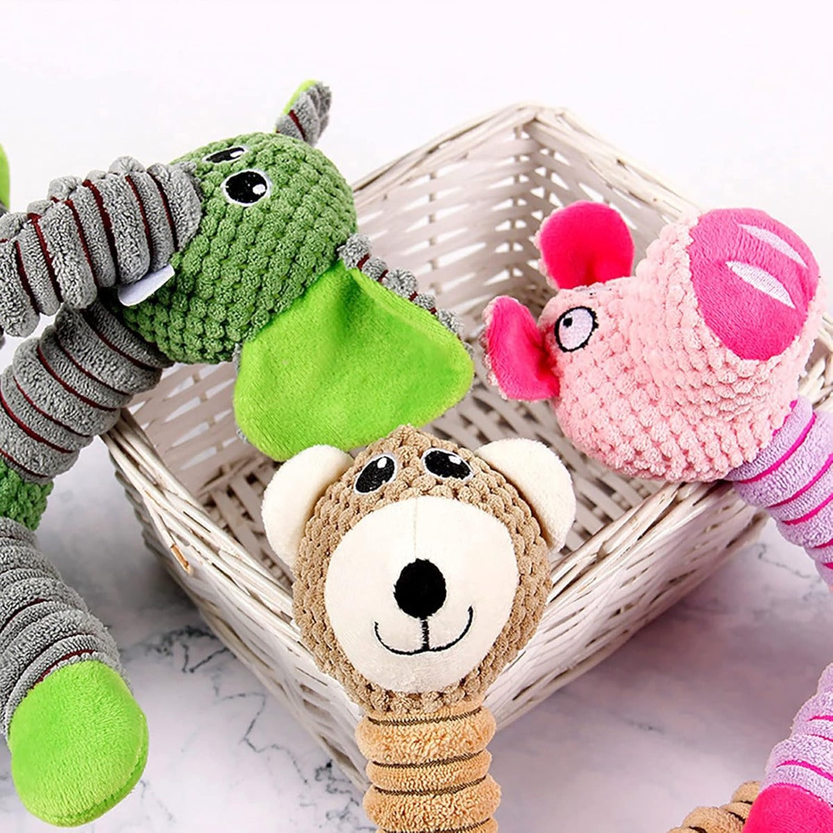 Giocattoli in peluche per cani in un cestino: elefante verde, maialino rosa e orsetto beige