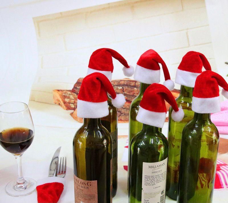 Mini cappelli Babbo Natale rossi con bordo bianco e pon pon, applicati su bottiglie e posate.