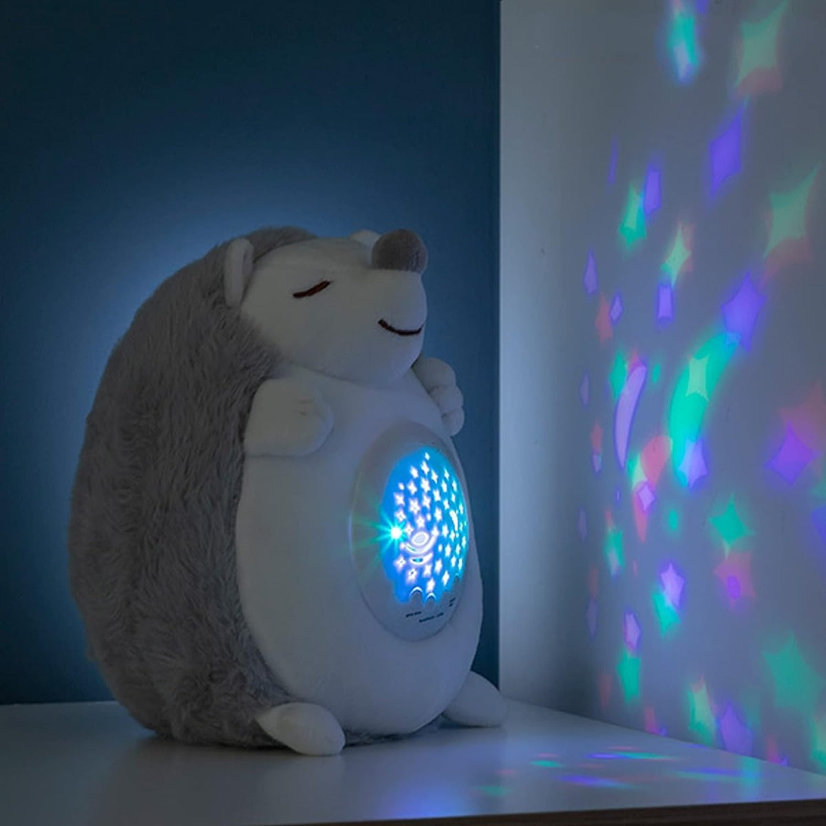 Riccio di peluche bianco e grigio con proiettore acceso e luce colorata dal pannello tondo