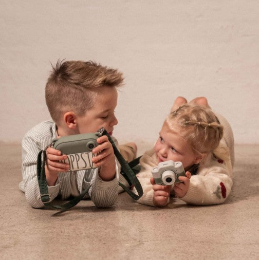 Fotocamera per bambini bianco-grigio con obiettivo, in mano a due bambini