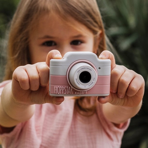 Fotocamera per bambini rosa tenue con obiettivo, tenuta da una bambina