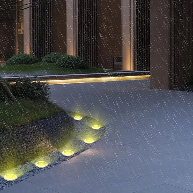 Faretti solari da incasso LED tondi accesi su vialetto, effetto pioggia