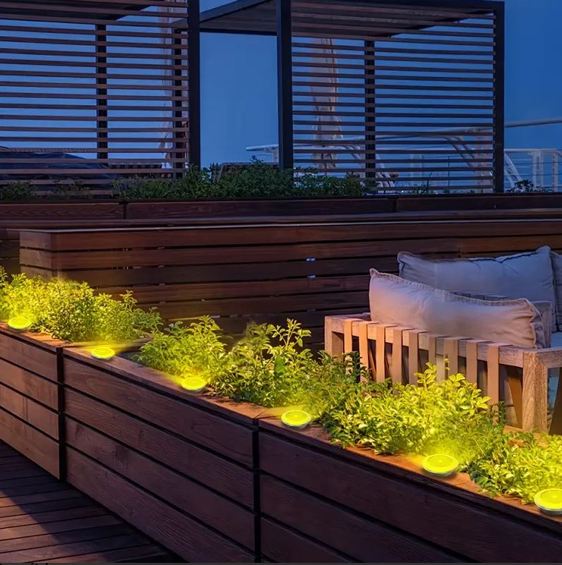Fascia di faretti solari da incasso LED tondi accesi lungo una fioriera
